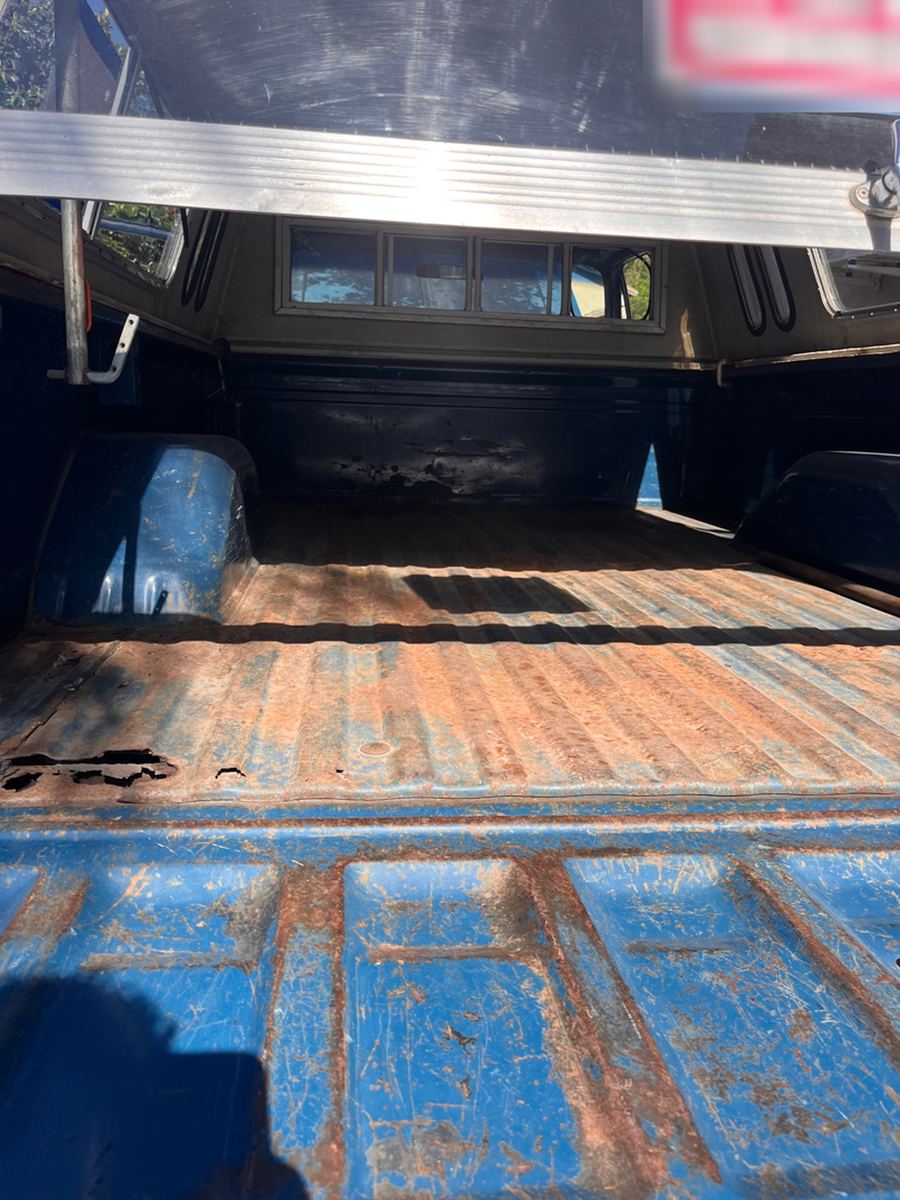 Pickup bed floor with surface rust under a camper shell, seller sign blurred out