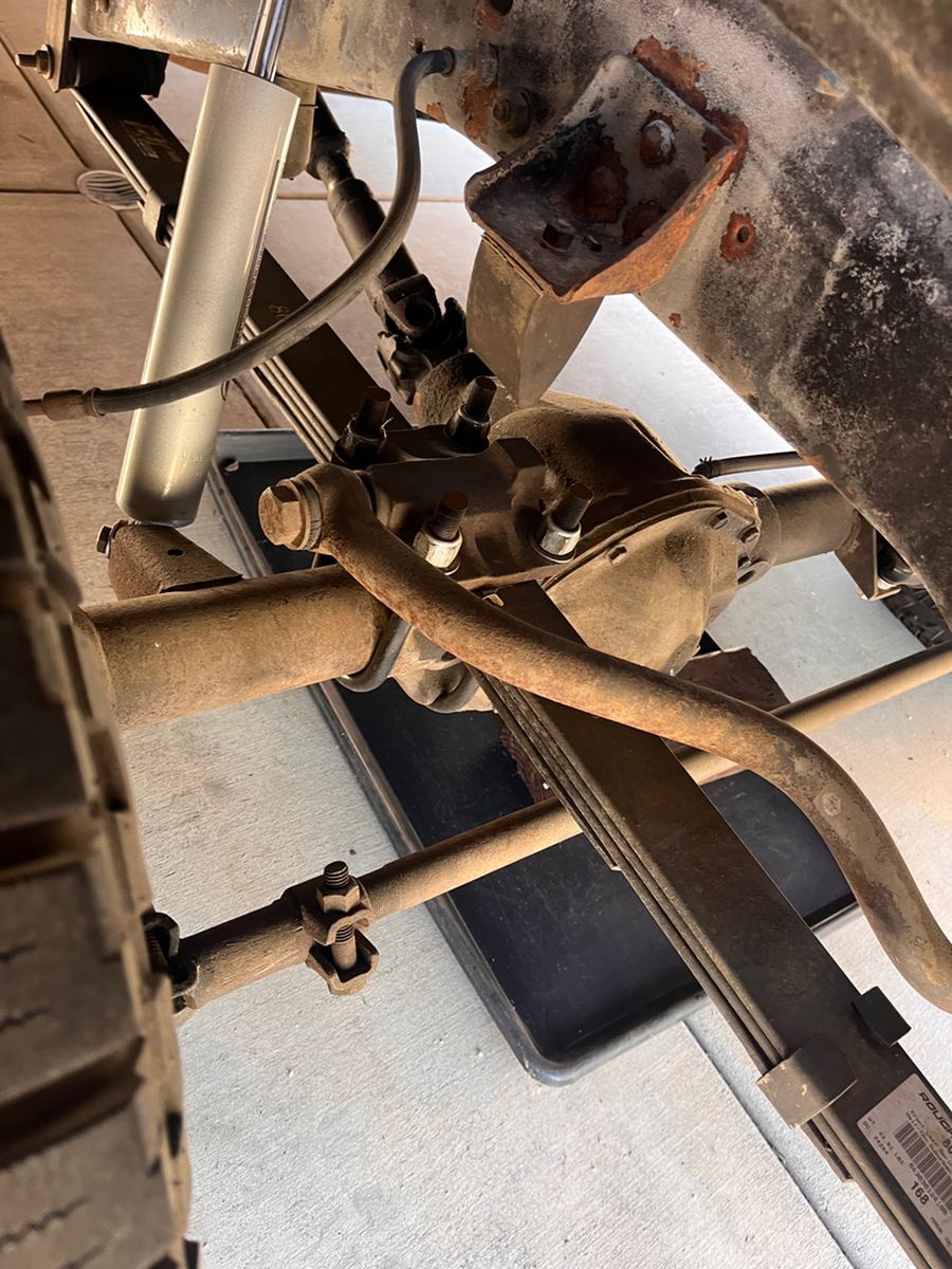 Front axle, leaf spring and steering linkage on a four-wheel-drive pickup, seen from below
