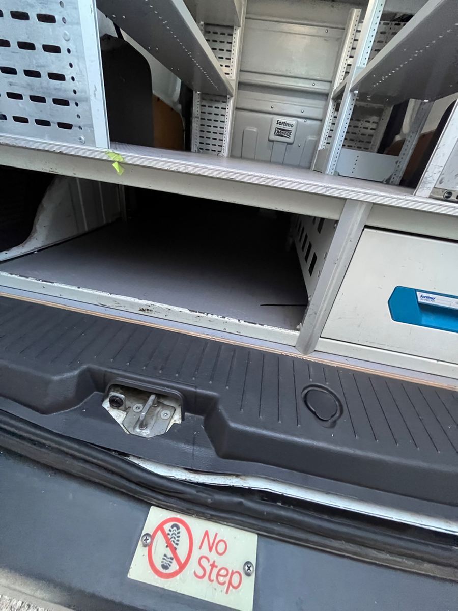 Rear load floor and bumper step of a cargo van seen through the open rear doors