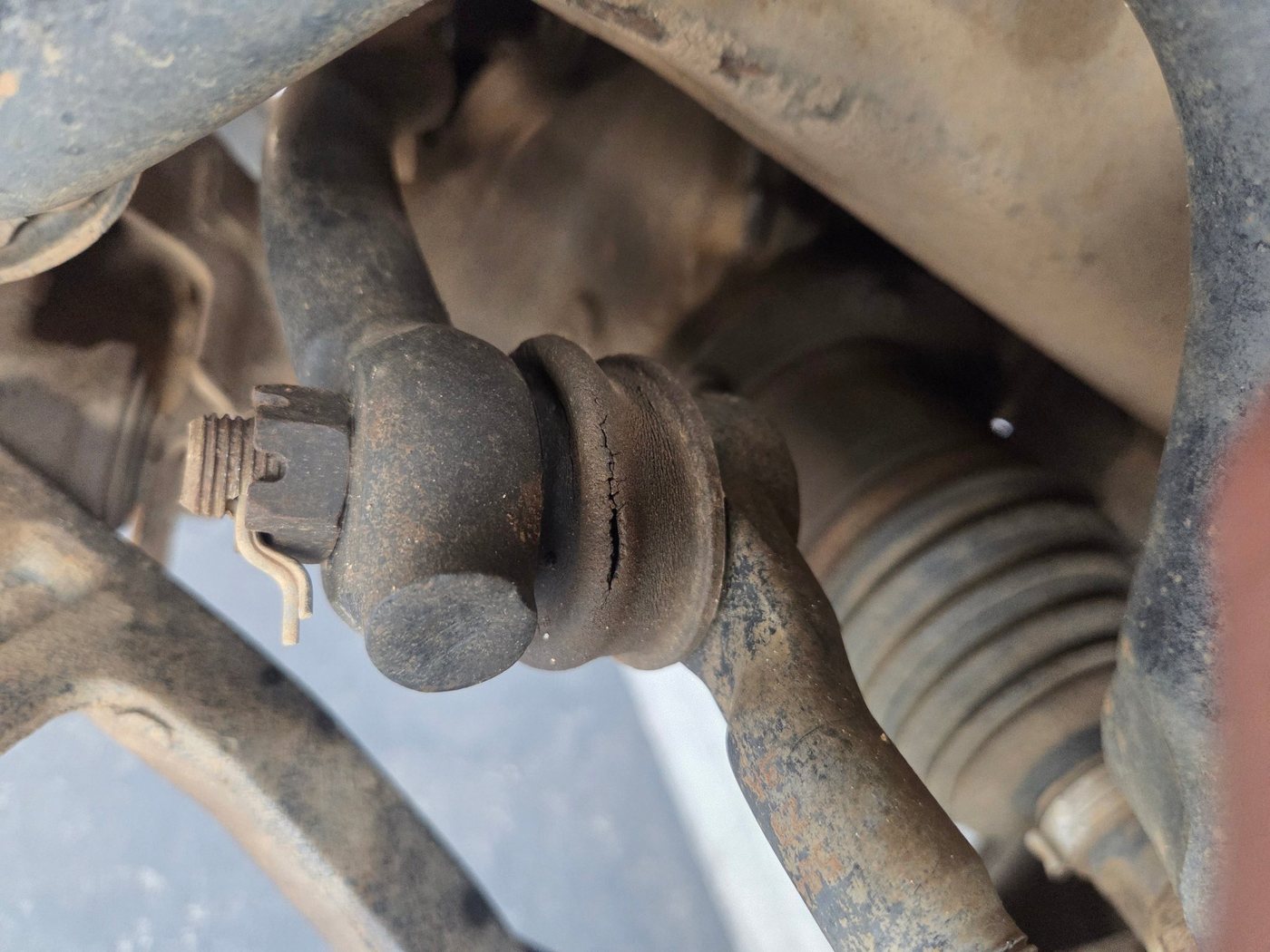 Outer tie rod end on a pickup, its rubber boot cracked and dirty