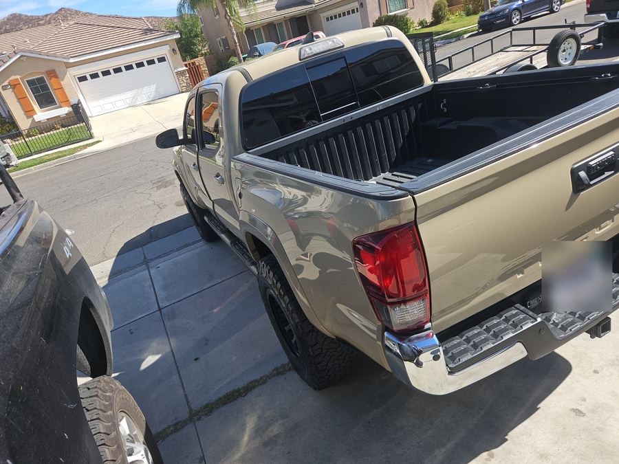 Tan Toyota Tacoma pickup seen from the rear corner with the bed liner in view