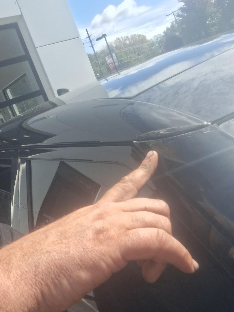 Inspector pointing at a rough spot on the edge of a black SUV roof spoiler