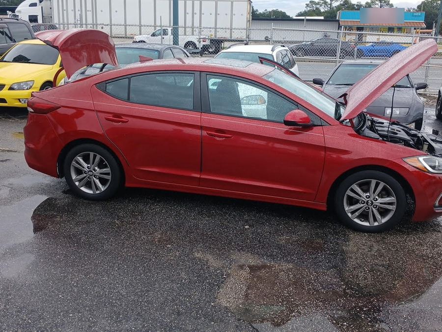 Red Hyundai Elantra sedan with the hood up on a wet dealer lot