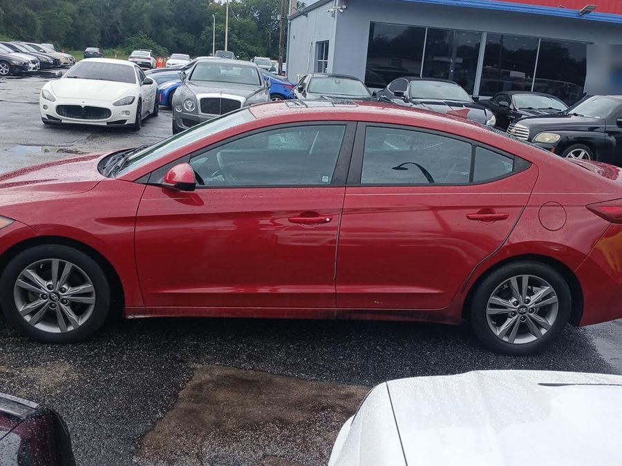 Driver side of a red Hyundai Elantra on a dealer lot after rain