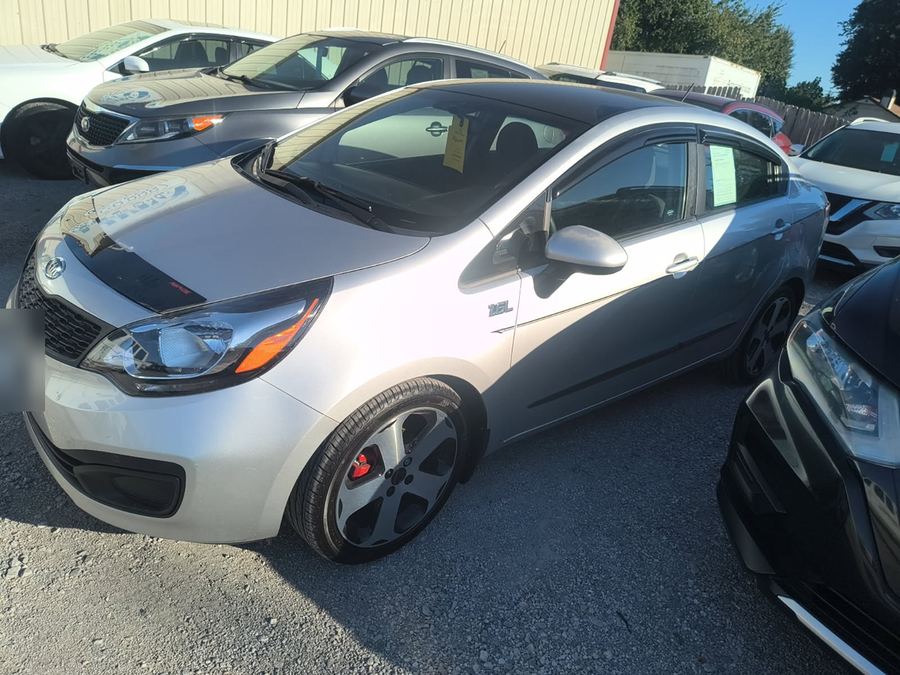 Silver Kia Rio sedan parked on a used car lot, seen from the front three-quarter
