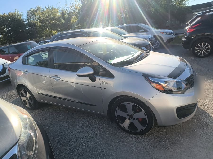 Kia Rio sedan on a gravel dealer lot with the low sun behind it