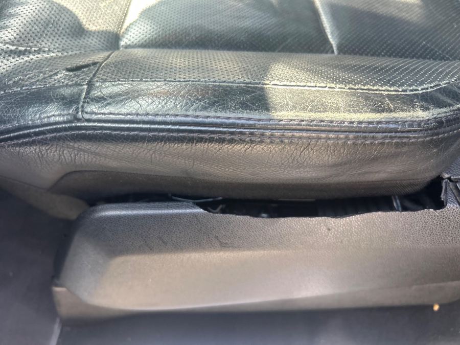 Black leather seat cushion with a broken plastic trim piece below it