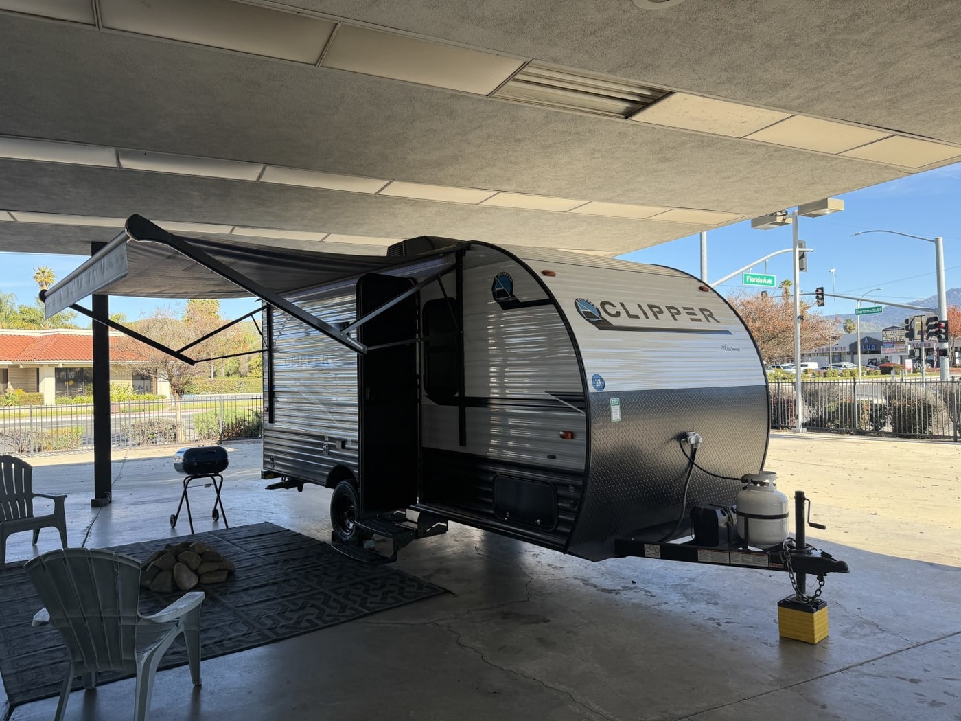 Small Coachmen Clipper travel trailer with its awning out under a covered lot