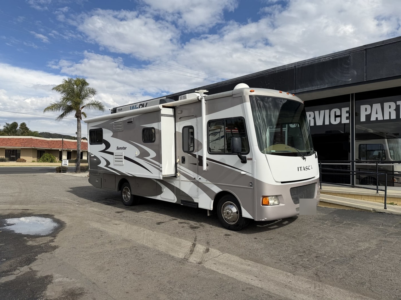 Itasca Sunstar Class A motorhome parked in front of a service building, plate blurred