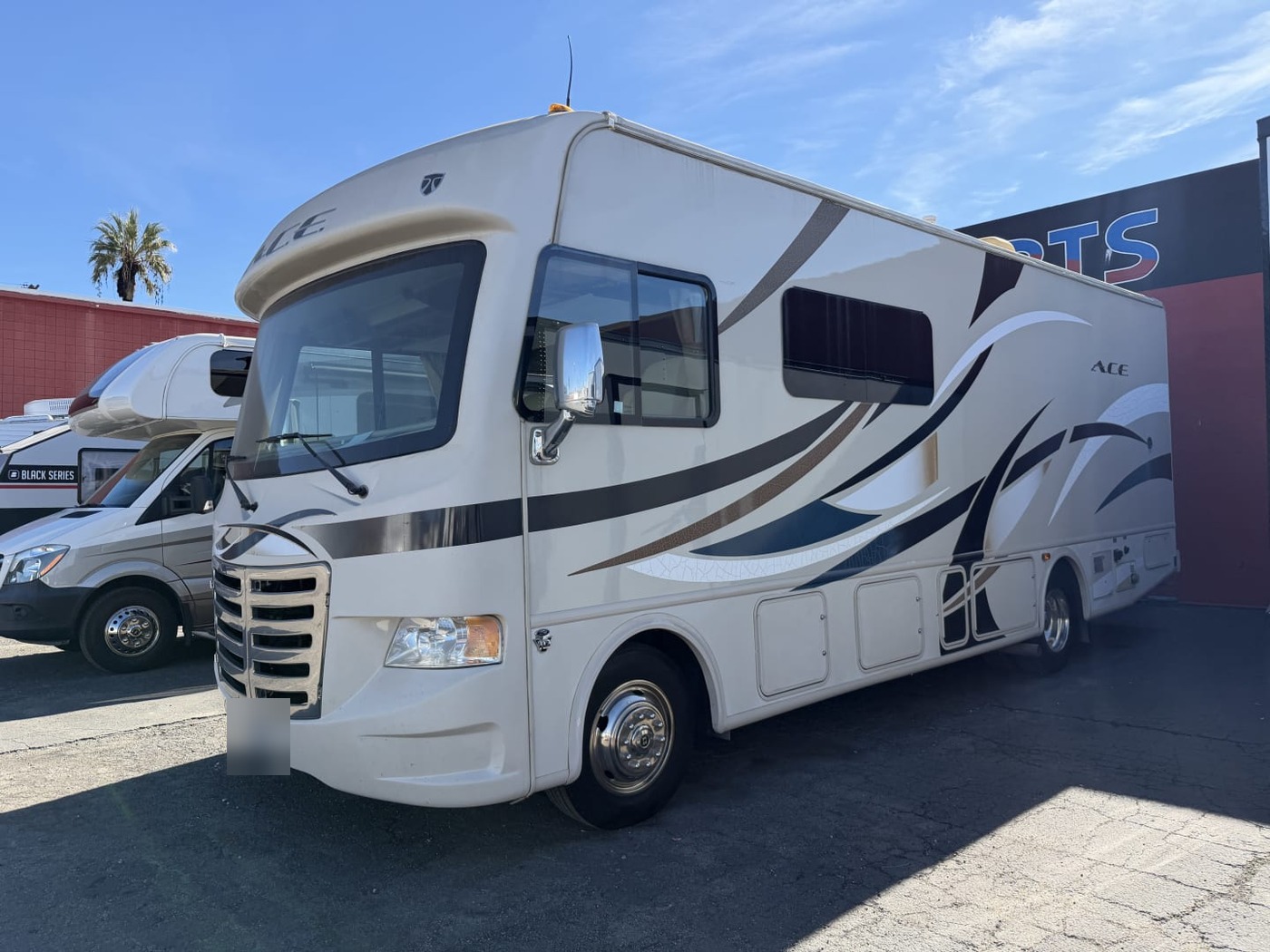 Front three-quarter view of a tan Thor A.C.E. Class A motorhome on a lot, plate blurred