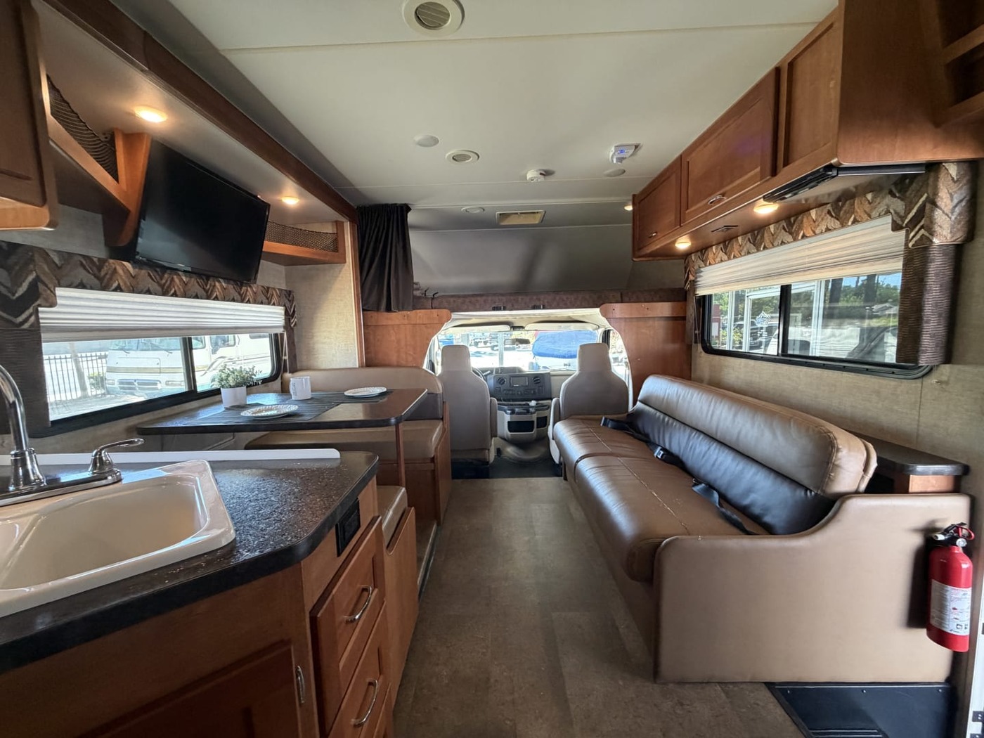 Inside a Class C motorhome looking forward past the sink, sofa and dinette to the cab