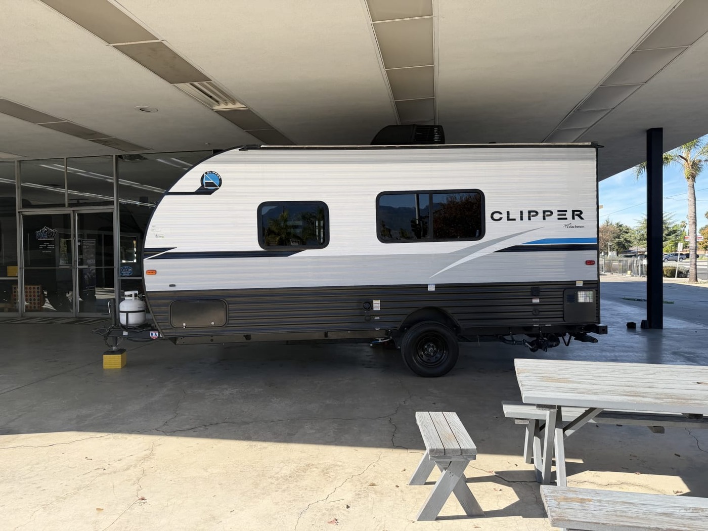 Side view of a small single-axle Coachmen Clipper travel trailer under a carport