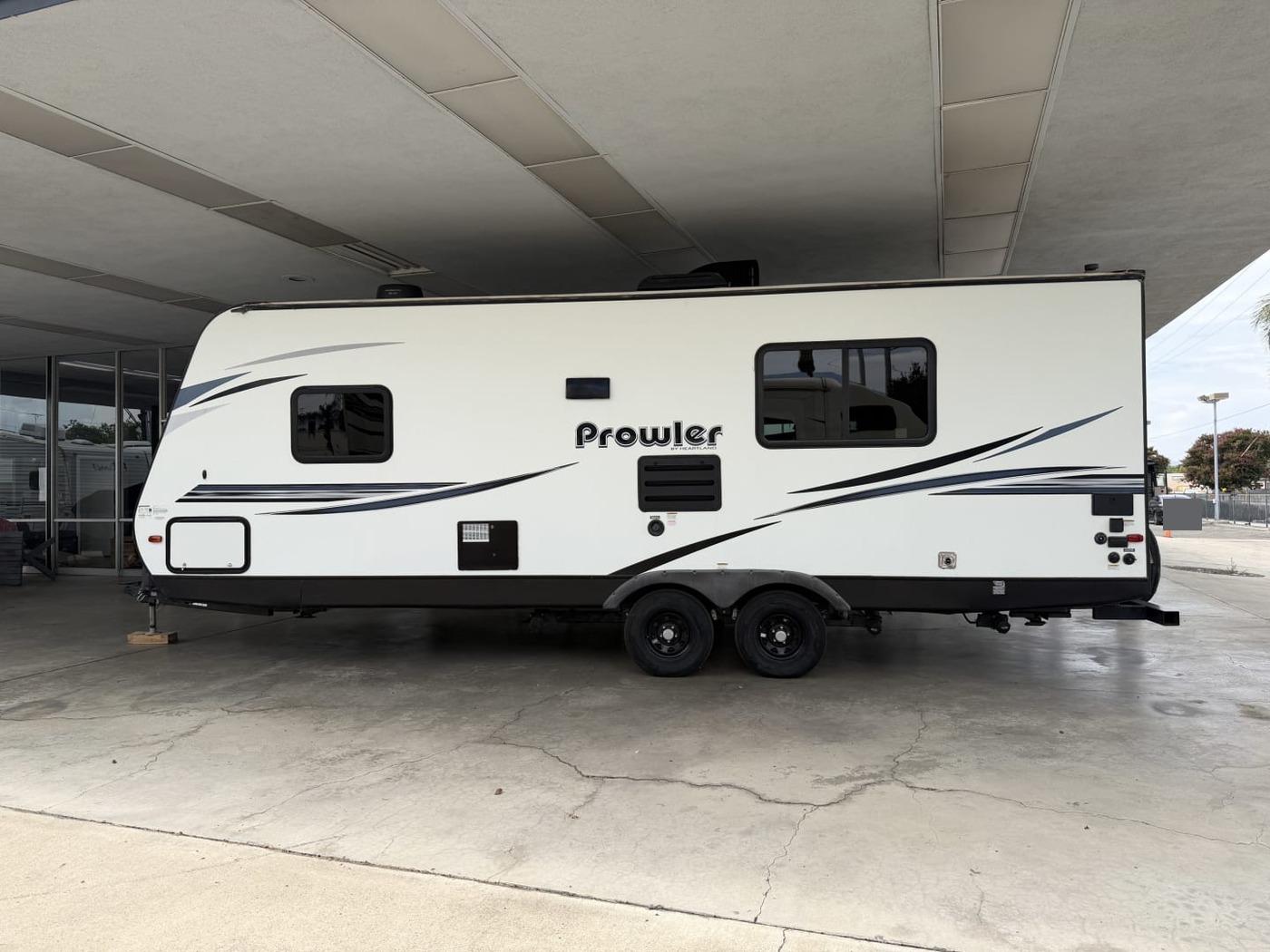 Side view of a Heartland Prowler tandem-axle travel trailer under a carport