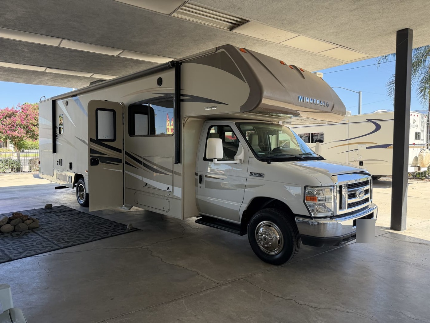 White and tan Winnebago Class C motorhome under a covered lot with its entry door open