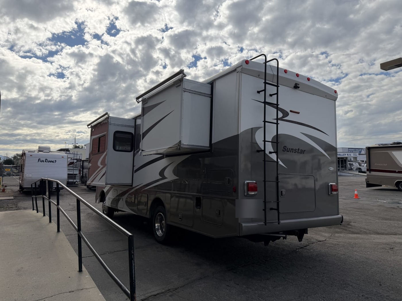 Rear of an Itasca Sunstar Class A motorhome with two slide-outs extended and a ladder to the roof, plate blurred