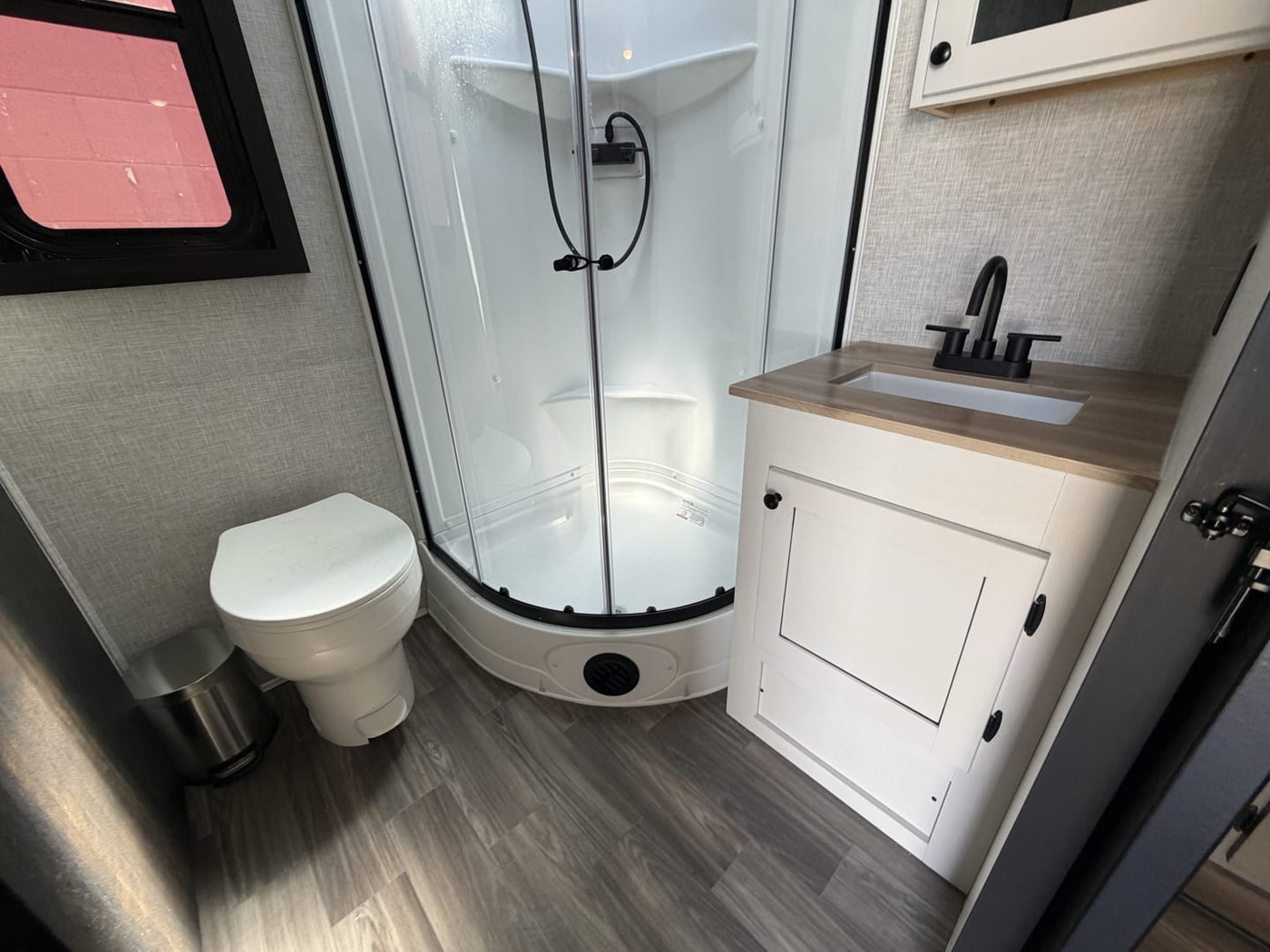 Travel trailer bathroom with a corner shower, toilet and vanity sink