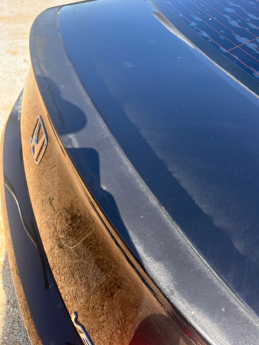 Peeling, faded clear coat across the trunk lid of a black Honda