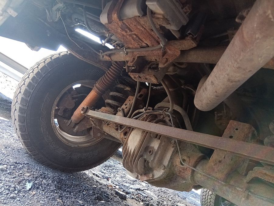 Rusty rear axle, leaf spring and shock seen from under an SUV