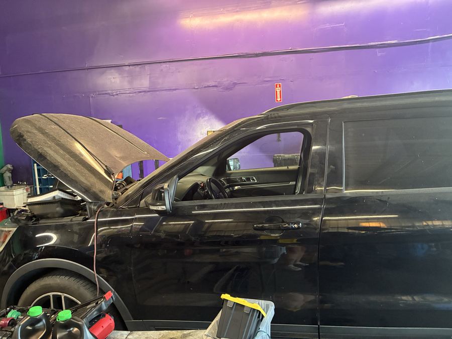 A black Ford Explorer in a workshop bay with its hood open and the front wheel removed